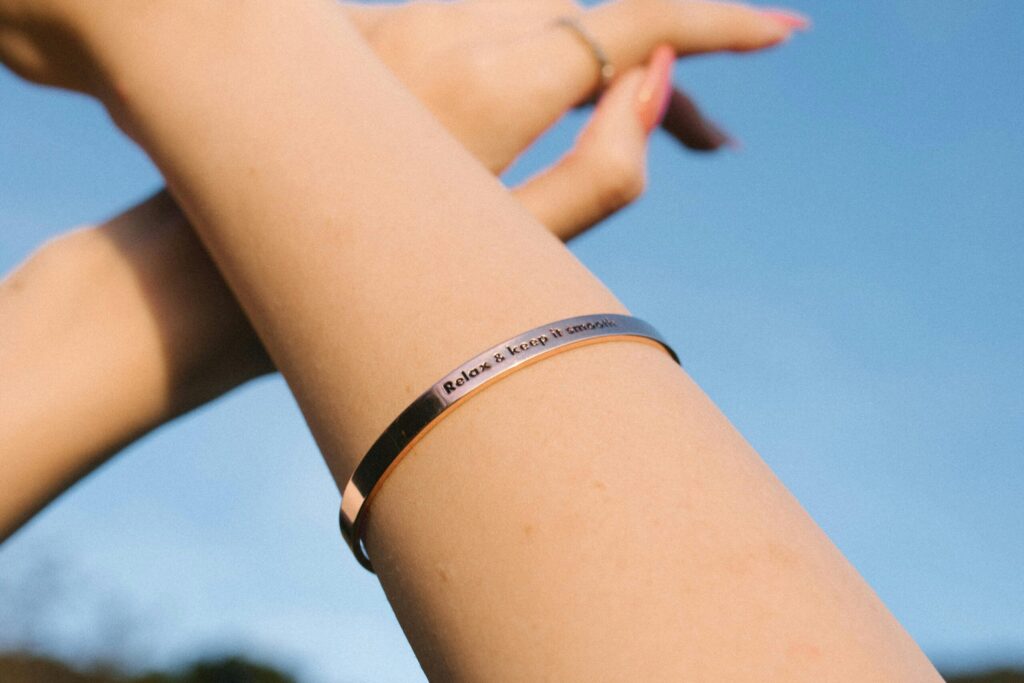 A close-up of an arm with a bracelet reading 'Relax & keep it simple' against a blue sky.